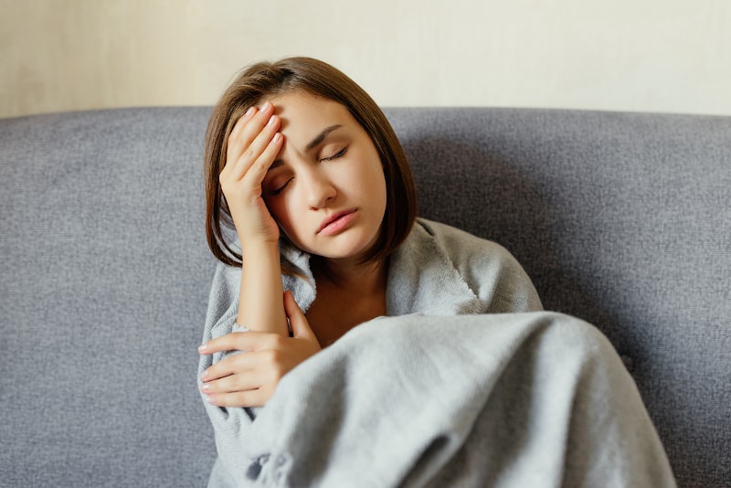 tired woman wrapped in blanket on couch